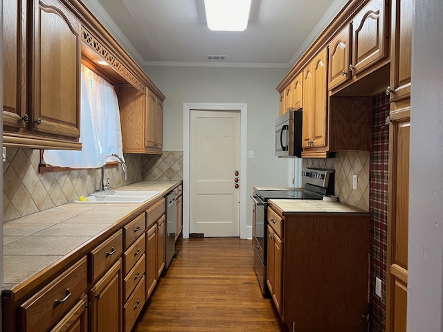 kitchen featuring stainless steel appliances, sink, tile countertops, ornamental molding, and decorative backsplash