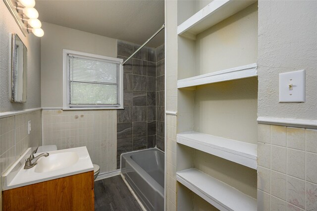 full bathroom with vanity, wood-type flooring, tile walls, built in shelves, and tiled shower / bath