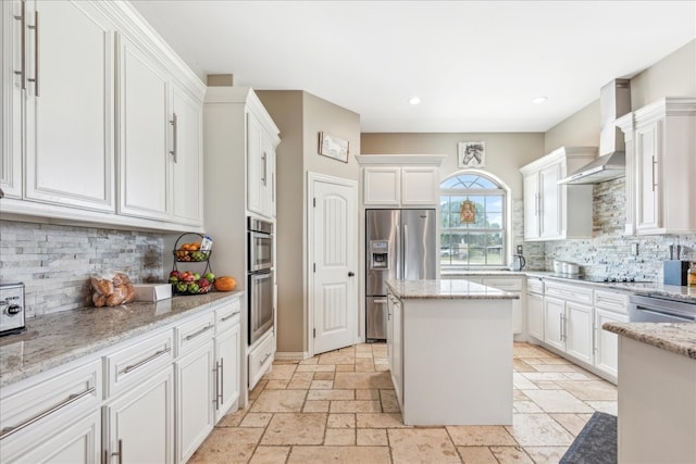 kitchen featuring white cabinetry, tasteful backsplash, a center island, wall chimney exhaust hood, and appliances with stainless steel finishes