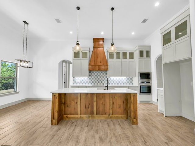 kitchen featuring white cabinets, premium range hood, light hardwood / wood-style floors, a spacious island, and appliances with stainless steel finishes