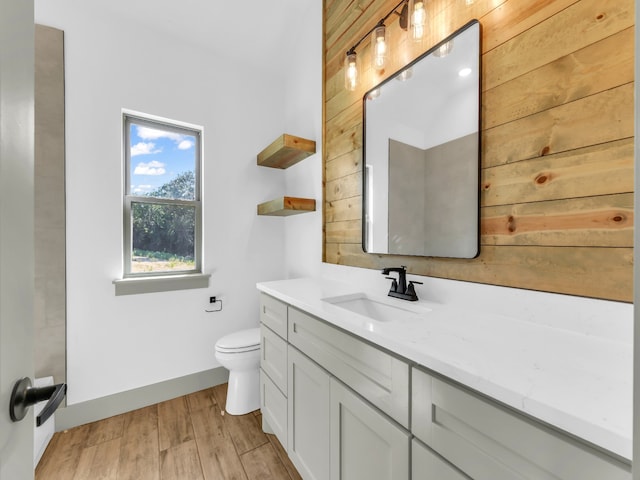 bathroom featuring wood-type flooring, wooden walls, vanity, and toilet