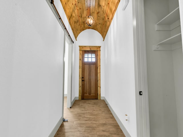 corridor with vaulted ceiling, a barn door, wooden ceiling, and light hardwood / wood-style flooring