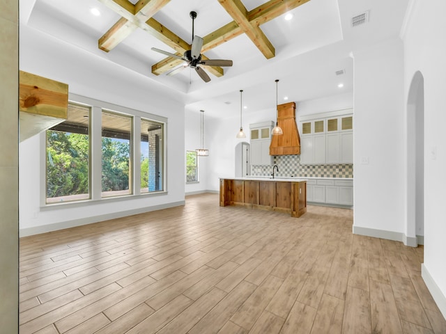 unfurnished living room with ceiling fan, beamed ceiling, sink, coffered ceiling, and light wood-type flooring