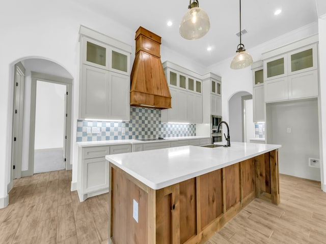 kitchen with pendant lighting, premium range hood, a kitchen island with sink, and white cabinetry