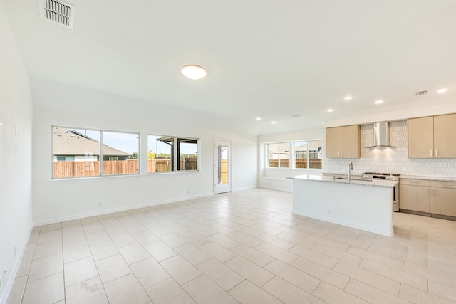 kitchen with wall chimney range hood, stainless steel gas range, plenty of natural light, and light brown cabinets