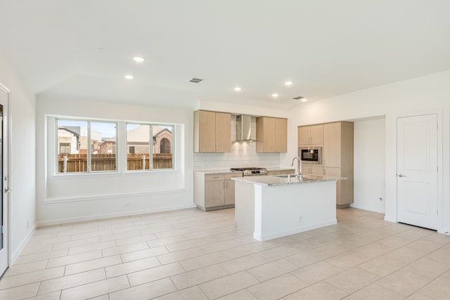 kitchen featuring wall chimney range hood, sink, stainless steel appliances, light brown cabinets, and a center island with sink