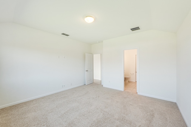 unfurnished bedroom featuring vaulted ceiling, light colored carpet, and ensuite bath