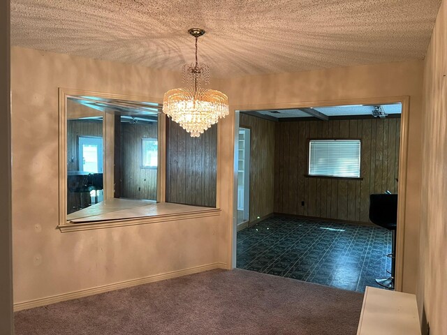 empty room with dark colored carpet, a textured ceiling, and a chandelier