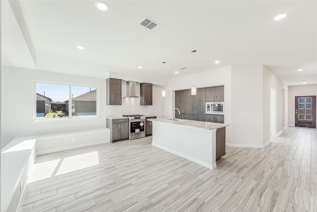 kitchen featuring pendant lighting, sink, wall chimney exhaust hood, light wood-type flooring, and stainless steel appliances