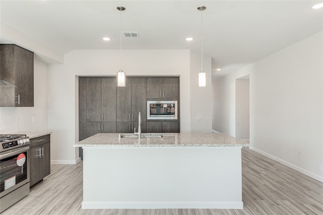 kitchen with light wood-type flooring, a kitchen island with sink, sink, pendant lighting, and stainless steel stove