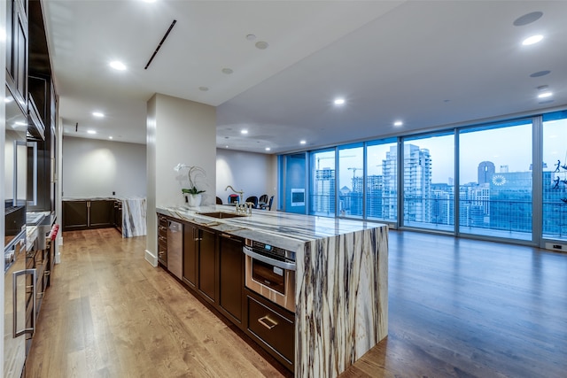 kitchen with sink, light wood-type flooring, stainless steel oven, light stone countertops, and a wall of windows