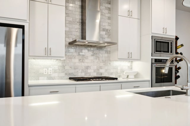 kitchen featuring wall chimney range hood, decorative backsplash, stainless steel appliances, and white cabinets