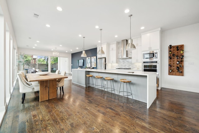 kitchen featuring white cabinets, a large island, dark hardwood / wood-style floors, stainless steel appliances, and wall chimney exhaust hood