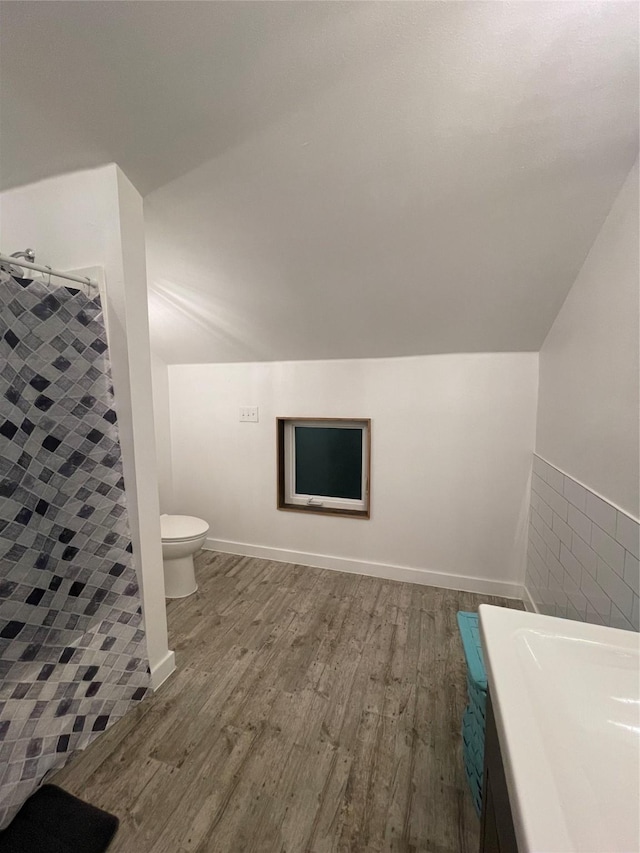 bathroom featuring lofted ceiling, wood-type flooring, a shower, tile walls, and toilet