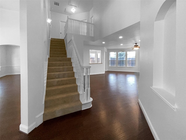 stairs with a towering ceiling, hardwood / wood-style floors, and ceiling fan