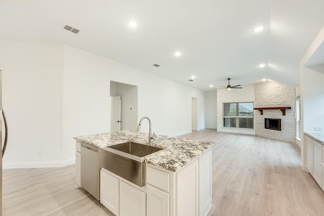 kitchen with stainless steel dishwasher, white cabinets, light wood-type flooring, and light stone counters