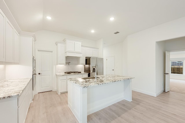 kitchen with light wood-type flooring, stainless steel appliances, a kitchen island with sink, sink, and white cabinetry