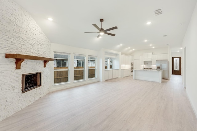 unfurnished living room featuring ceiling fan, light hardwood / wood-style floors, a stone fireplace, and vaulted ceiling