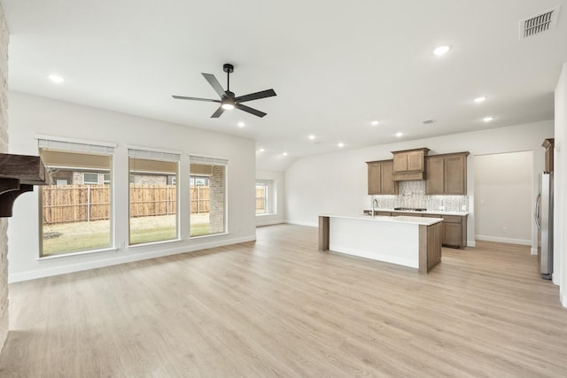 kitchen with stainless steel refrigerator, an island with sink, light hardwood / wood-style flooring, and backsplash