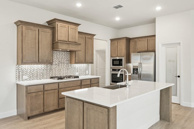 kitchen with sink, a center island with sink, appliances with stainless steel finishes, light hardwood / wood-style floors, and backsplash