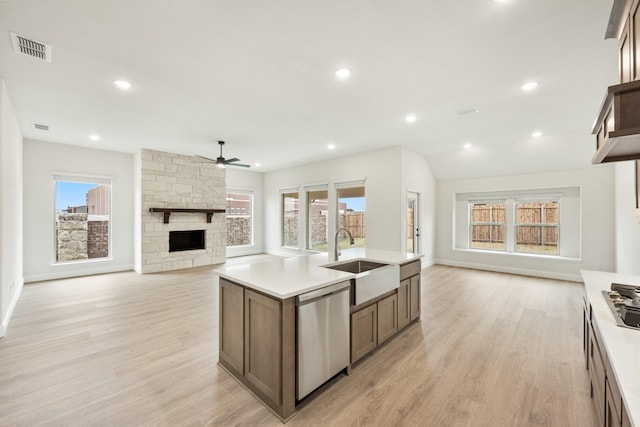 kitchen with appliances with stainless steel finishes, sink, a stone fireplace, and light hardwood / wood-style floors