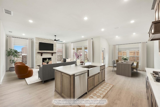 kitchen featuring sink, a kitchen island with sink, stainless steel appliances, a stone fireplace, and light wood-type flooring