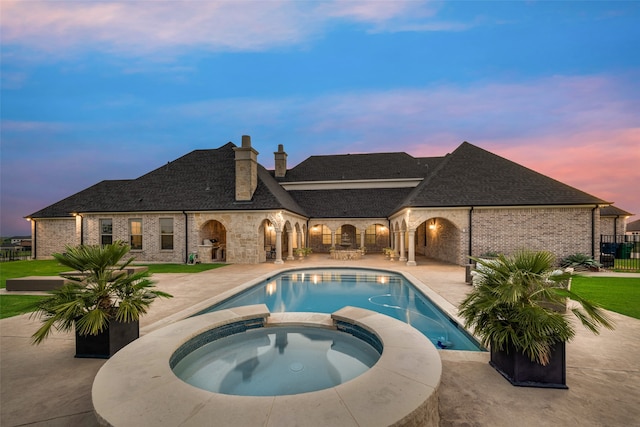 pool at dusk featuring an in ground hot tub and a patio