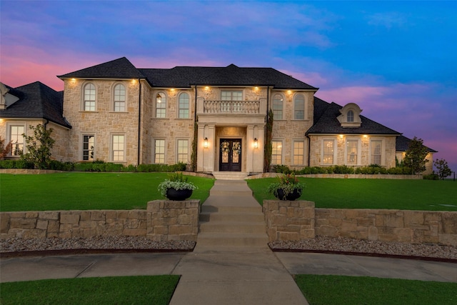 view of front of property featuring french doors, a balcony, stone siding, and a front lawn