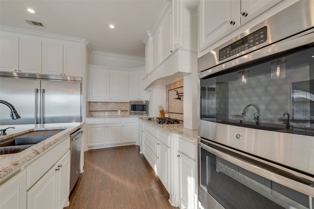 kitchen with light stone counters, built in appliances, decorative backsplash, and white cabinetry