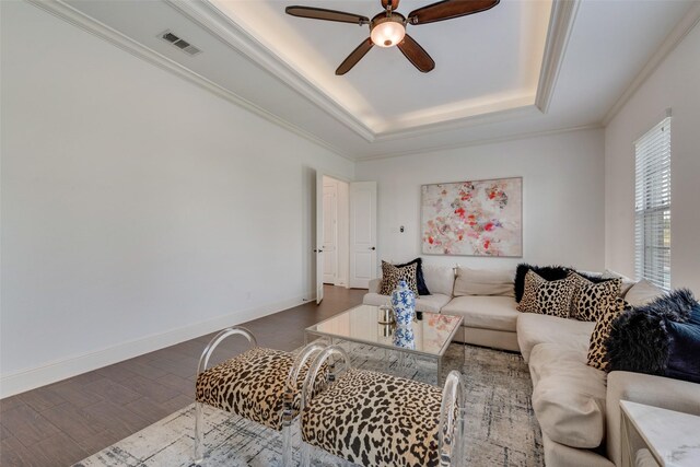 living room with ceiling fan, visible vents, wood finished floors, ornamental molding, and a tray ceiling