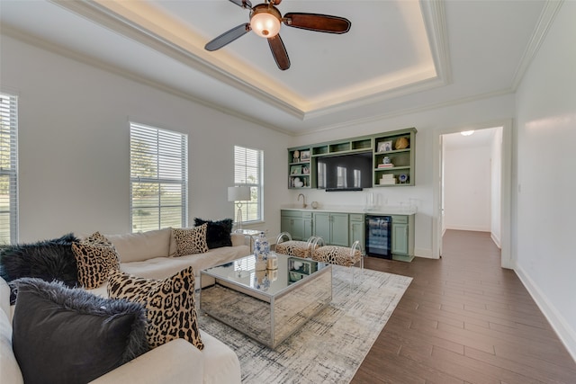 living room with ceiling fan, wine cooler, wood-type flooring, a tray ceiling, and bar area