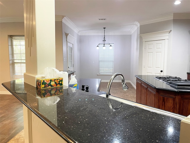 kitchen featuring dark stone counters, crown molding, hanging light fixtures, and light wood-type flooring