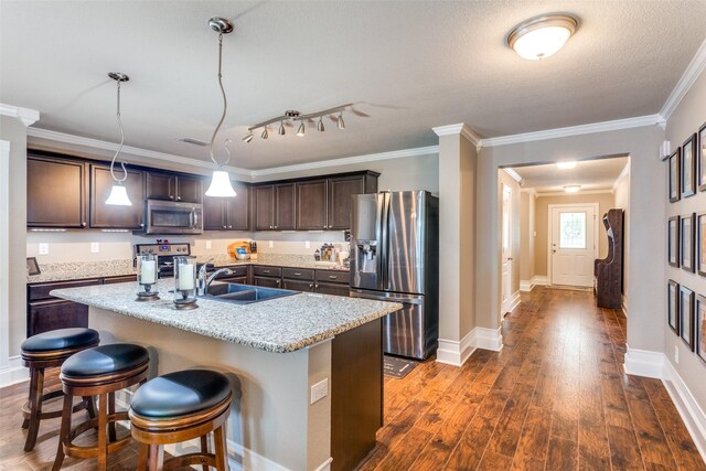 kitchen with stainless steel appliances, sink, dark hardwood / wood-style floors, decorative light fixtures, and an island with sink