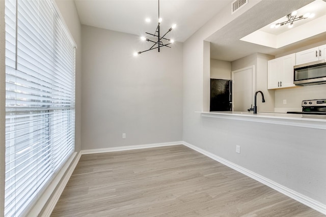 interior space with light wood finished floors, visible vents, appliances with stainless steel finishes, an inviting chandelier, and white cabinetry