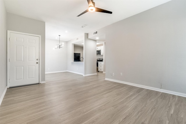 unfurnished living room with ceiling fan with notable chandelier, light wood finished floors, and baseboards