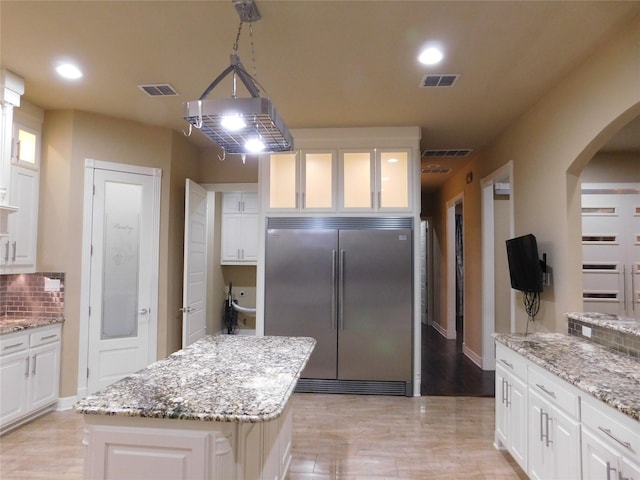 kitchen with built in fridge, arched walkways, glass insert cabinets, and visible vents