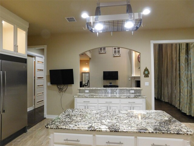 kitchen with white cabinets, a kitchen island, light stone counters, and built in refrigerator