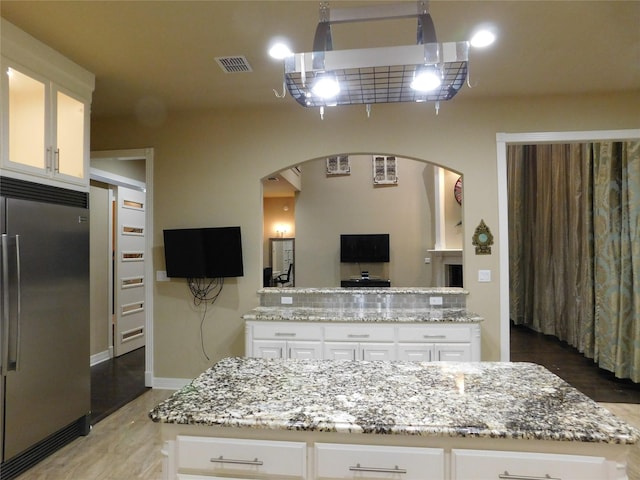 kitchen with stainless steel built in refrigerator, light stone countertops, arched walkways, white cabinetry, and a center island
