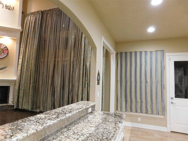 interior space featuring baseboards, wood finished floors, a fireplace with raised hearth, and recessed lighting