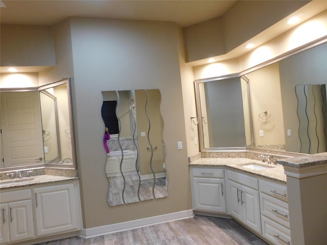 full bath with baseboards, a sink, two vanities, and wood finished floors