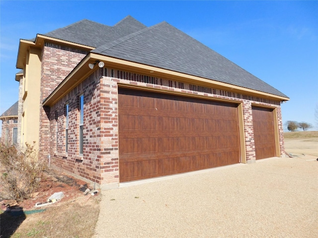 view of side of property featuring brick siding, a garage, concrete driveway, and a shingled roof