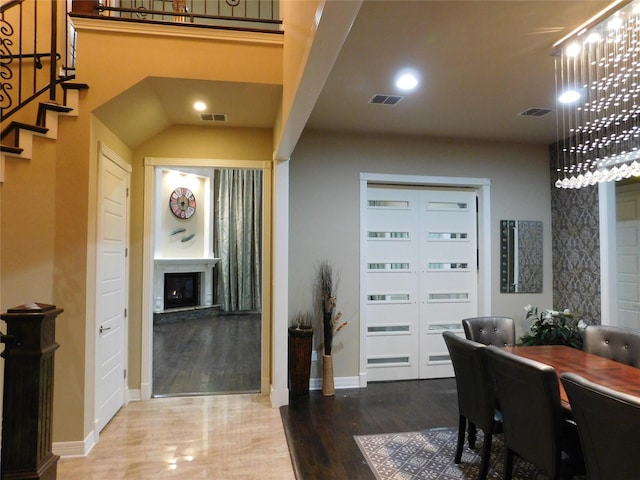 dining space with a fireplace with raised hearth, visible vents, stairway, and wood finished floors