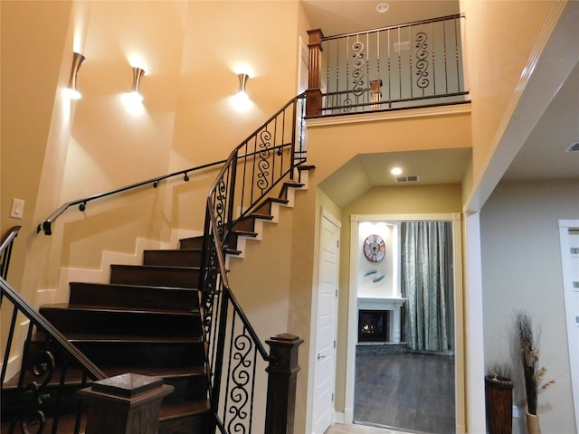 staircase featuring visible vents, a towering ceiling, and a fireplace