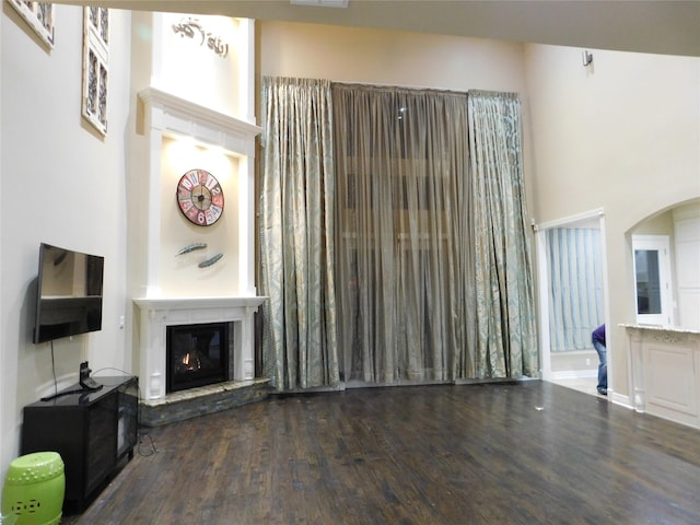 living room with arched walkways, a high ceiling, wood finished floors, and a glass covered fireplace