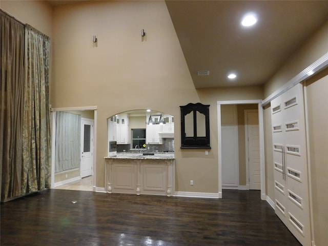 kitchen with tasteful backsplash, kitchen peninsula, white cabinetry, light stone countertops, and dark wood-type flooring