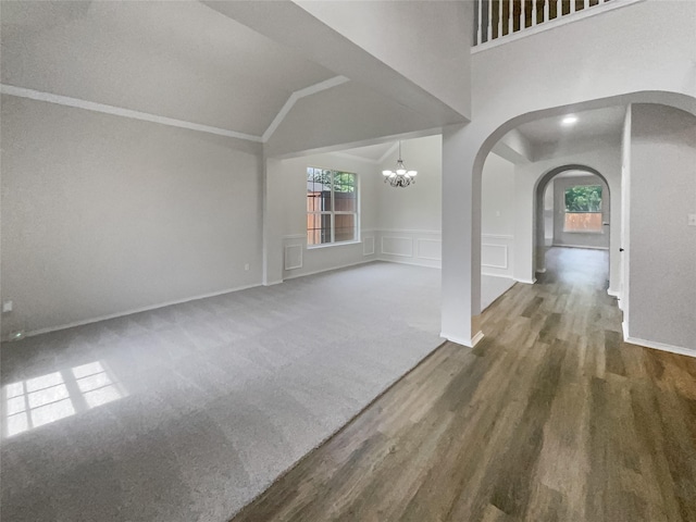 unfurnished living room featuring a notable chandelier, ornamental molding, dark wood-type flooring, and vaulted ceiling