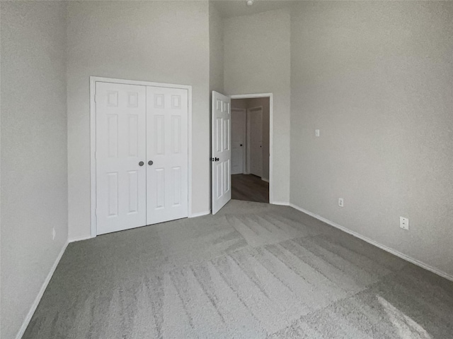 unfurnished bedroom featuring a towering ceiling, a closet, and carpet