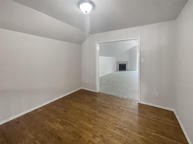 additional living space with dark hardwood / wood-style flooring, a tile fireplace, and vaulted ceiling