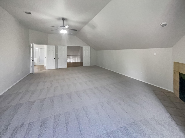 additional living space featuring a tiled fireplace, ceiling fan, light colored carpet, and vaulted ceiling