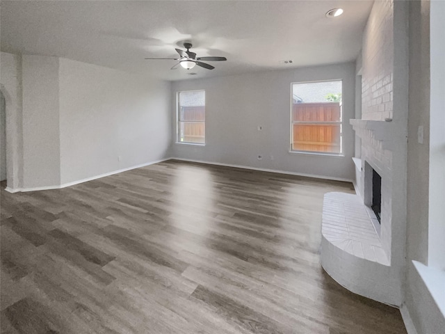 unfurnished living room featuring ceiling fan, dark wood-type flooring, and a brick fireplace